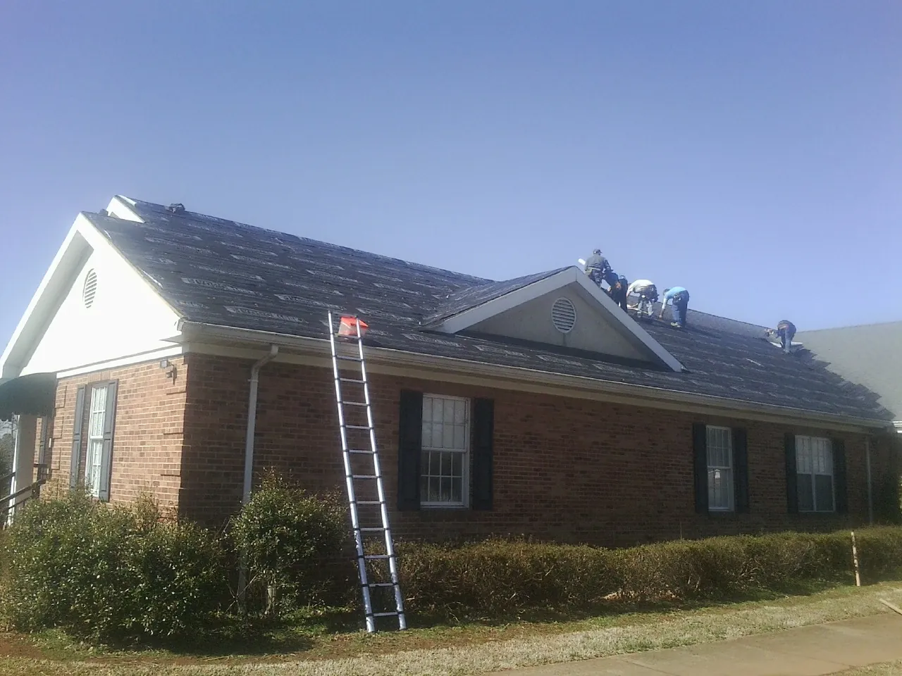 Crew tearing shingles off a brick ranch roof with a ladder set — Metal Roof Repair work by our crew in White Sulphur Springs