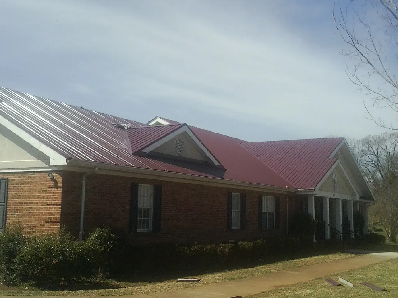 Red metal roof with gabled entries on a long brick building, from a Hail Damage Roof Repair job in White Sulphur Springs
