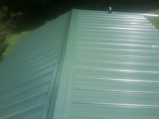 New green metal panels meeting at the ridge of a roof — Flat Roof Repair work by our crew in White Sulphur Springs