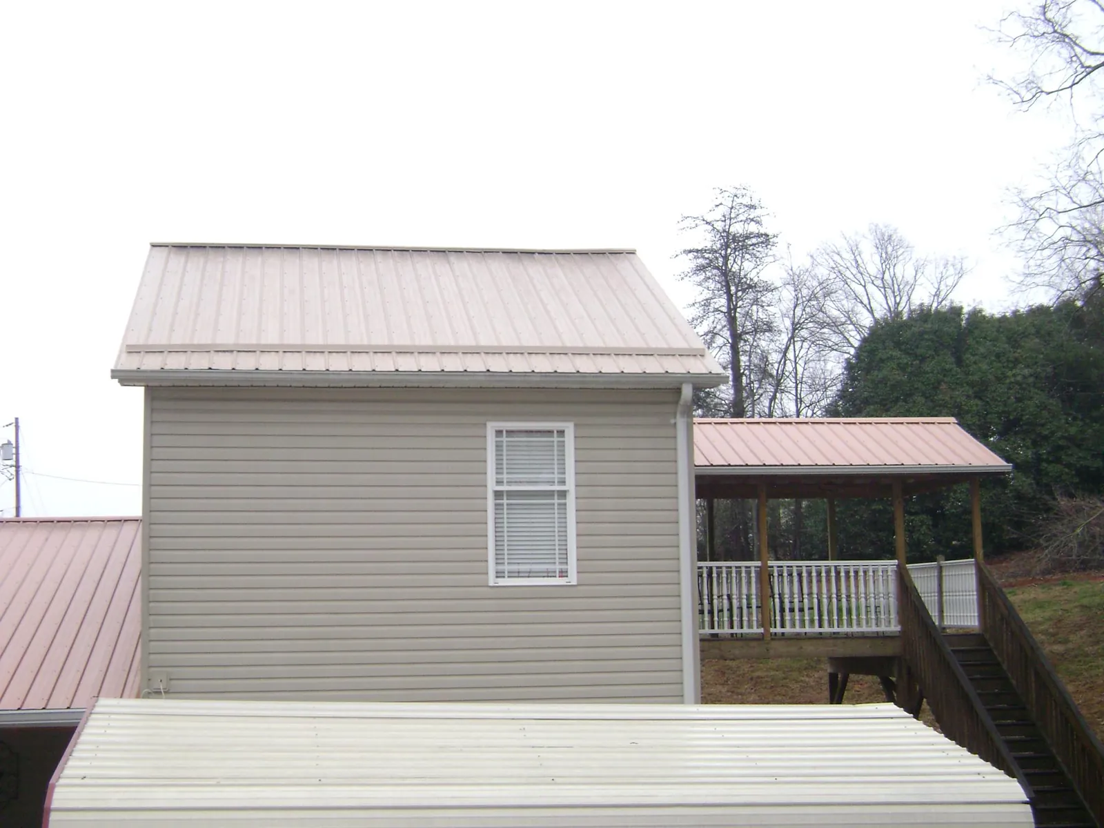 Tan metal roofs on a two story addition and attached porch, from a Roof Replacement job in White Sulphur Springs